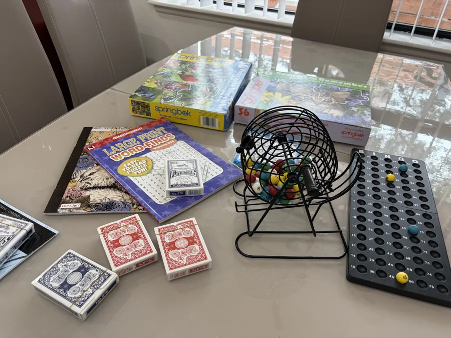 A bingo cage and board, jigsaw puzzles, a large-print word search and packs of playing cards on the dining table