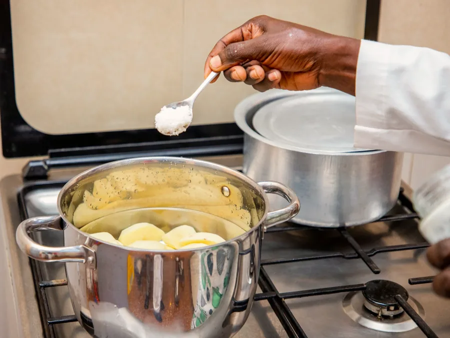 A hand seasoning a pot of potatoes cooking on the stove