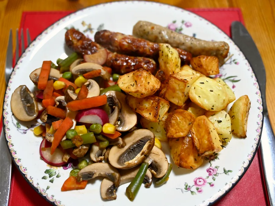 A dinner of sausages, roast potatoes and mixed vegetables on a plate