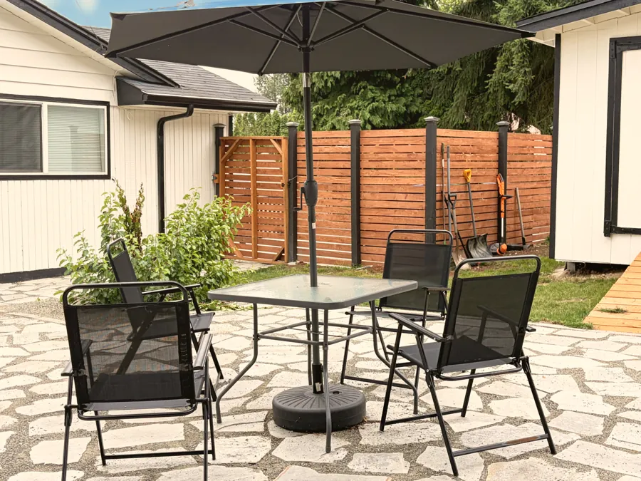 A paved back patio with a table, chairs and a large umbrella